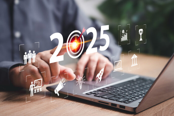 Businessperson sits in front of a laptop which visually projects a 2025 with a target in the middle of the 0