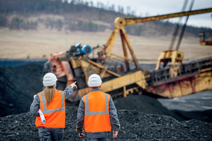 Monitoring to Prevent Patterns of Violations: two mine workers in orange safety vest overlooking a coal operation.